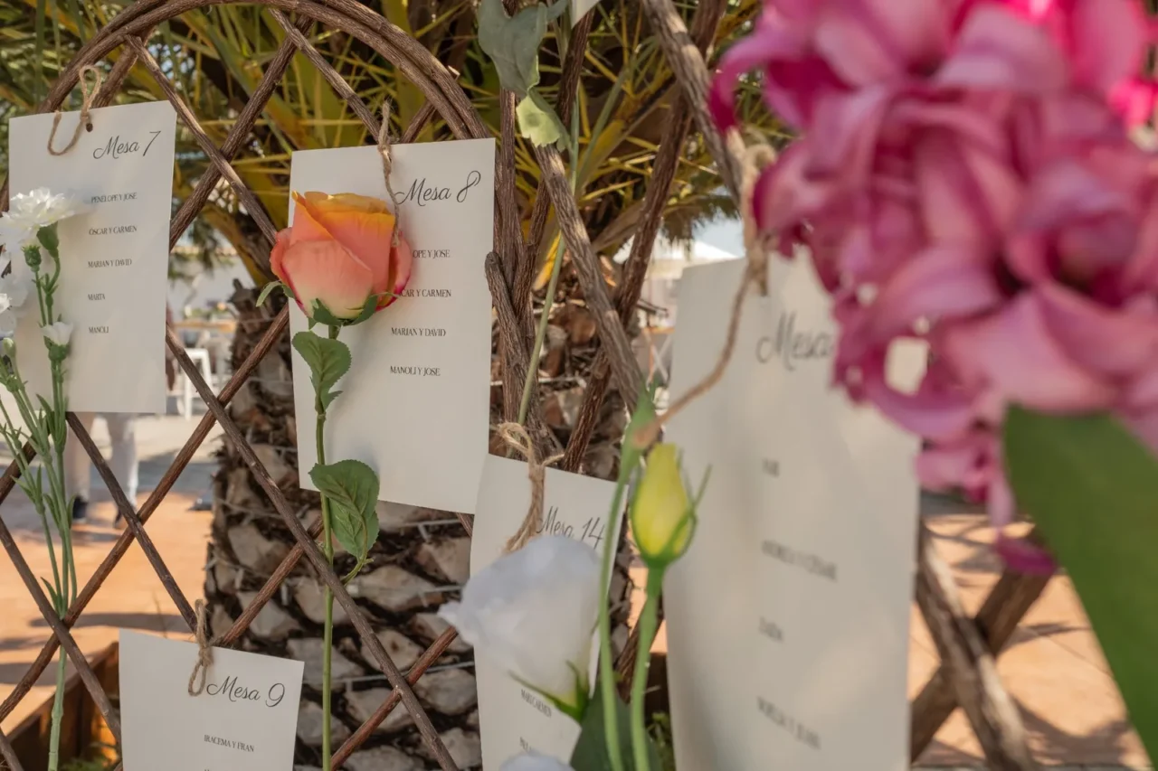Detalle de flores rosas y tarjetas del seating plan colgadas de una estructura de madera en una boda