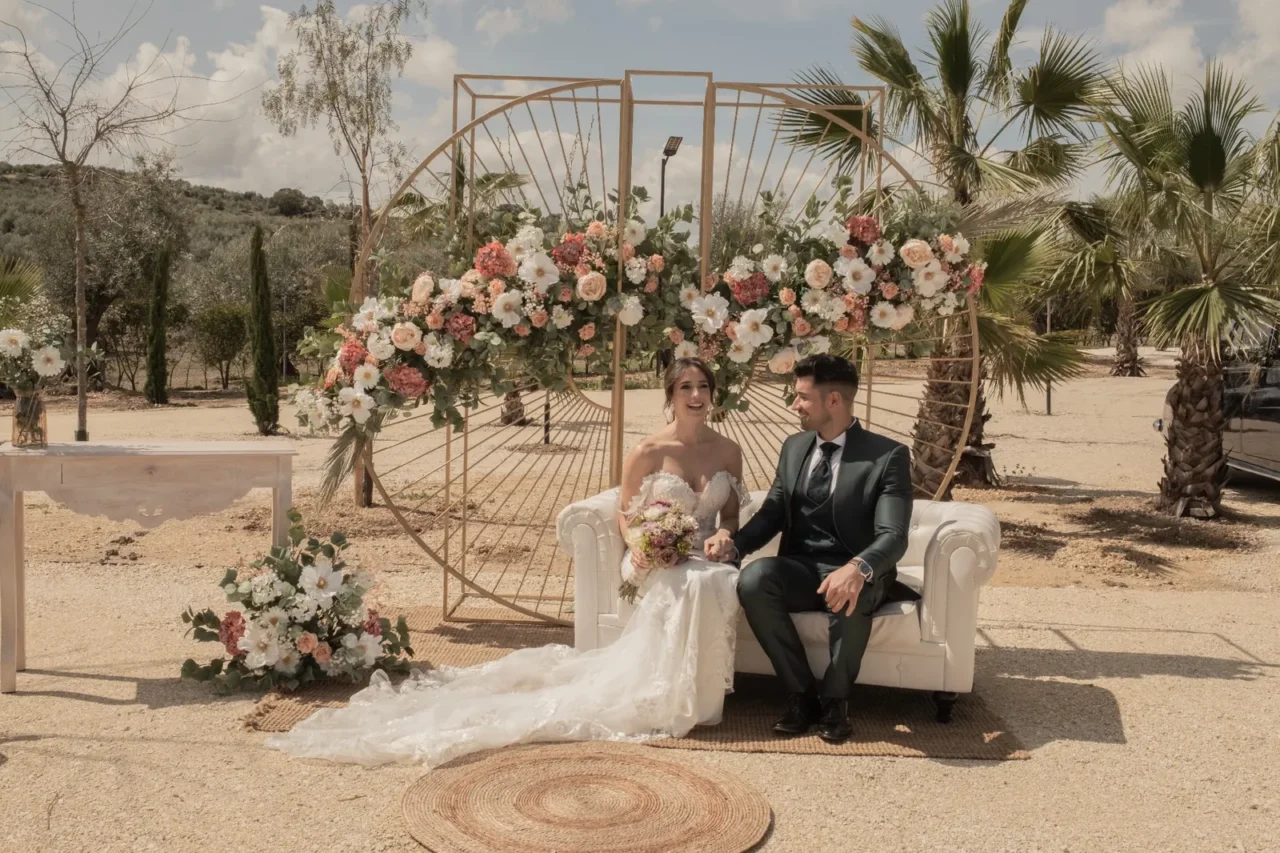 Novia con vestido blanco junto a su pareja en una ceremonia exterior con estructura floral