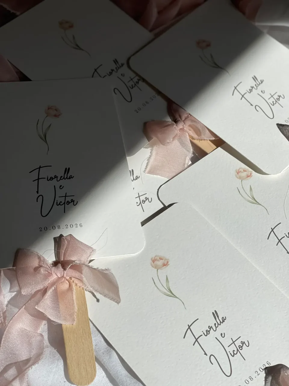 Paipáis personalizados con nombres de Fiorella y Víctor y lazos de tela rosa, dispuestos sobre una superficie clara